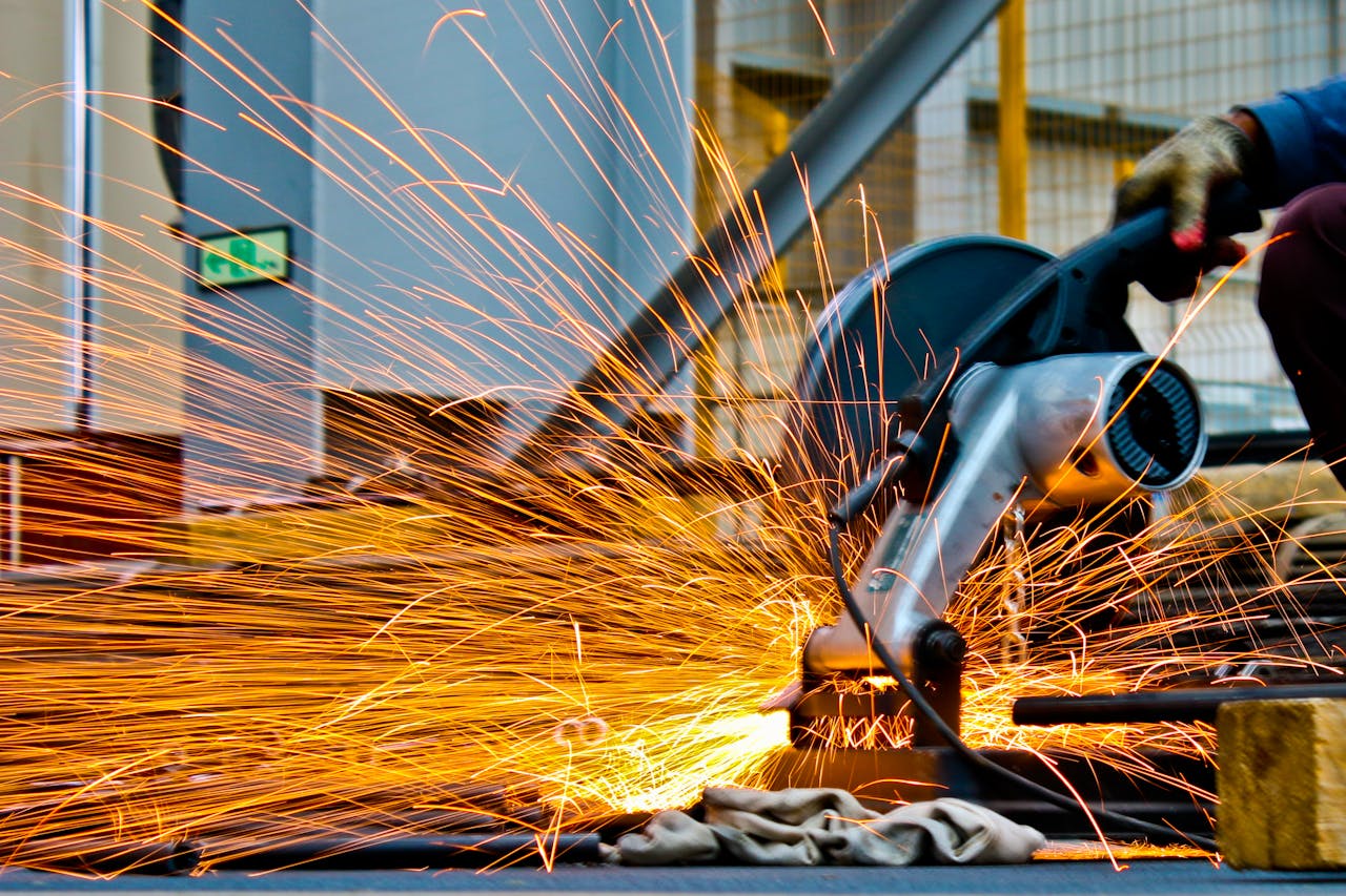 Home A worker operates a grinder cutting metal, creating a vibrant display of sparks in an industrial setting.